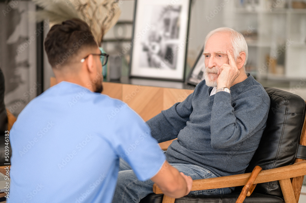 Despondent pensioner seated in the room before his caretaker