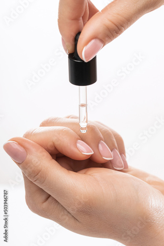 Female hands and bottle of nourishing cuticle oil with a dropper photo