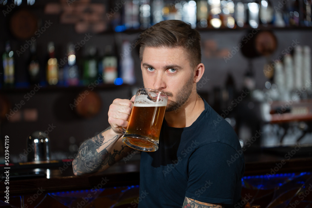 Young man sitting at bar counter with a pint of light beer