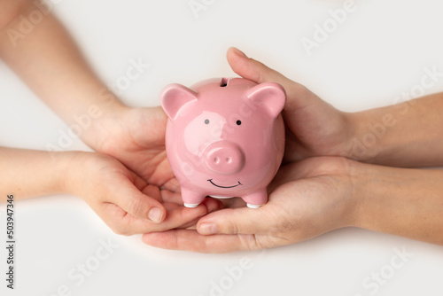 A woman and child holding a piggy bank in the shape of a pink pig, she is organizing money to divide it into savings and buy funds to make it grow. Personal finance concept