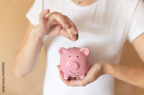 Female hands puts a coin in a pink piggy bank. The concept of saving money or savings, investment