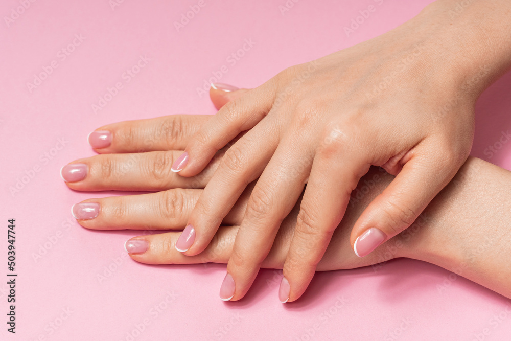 Female hands with soft skin and beautiful french manicure against pink background