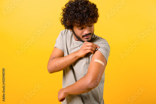 Bilde på lerret Curly Indian man with medical band-aid on arm after the vaccination looking at i