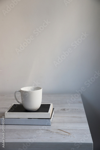 A white cup of tea on modern white and black books on a beige kitchen table.