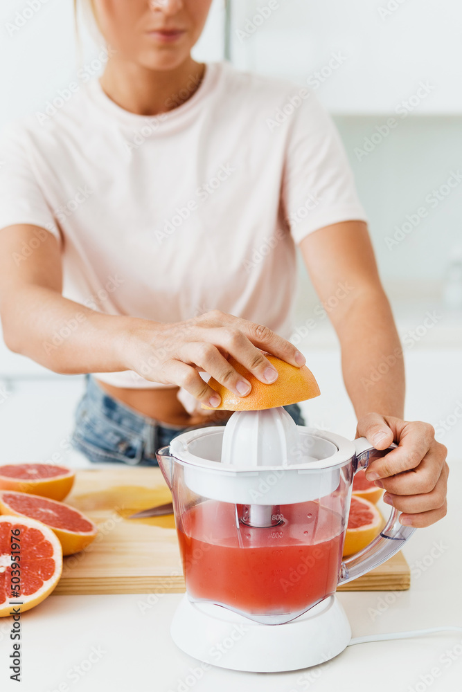 Female hands and citrus juicer during fresh grapefruit juice preparation - obrazy, fototapety, plakaty 