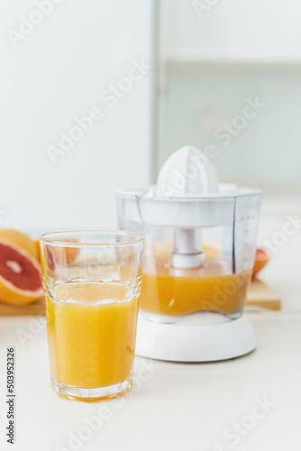 Glass of orange juice, citrus juicer and various citrus fruits on kitchen table