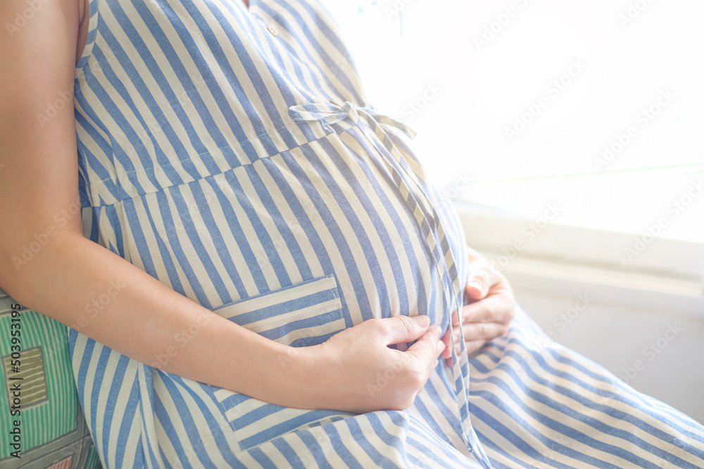 Pregnant woman touching her swollen belly and sitting near the window