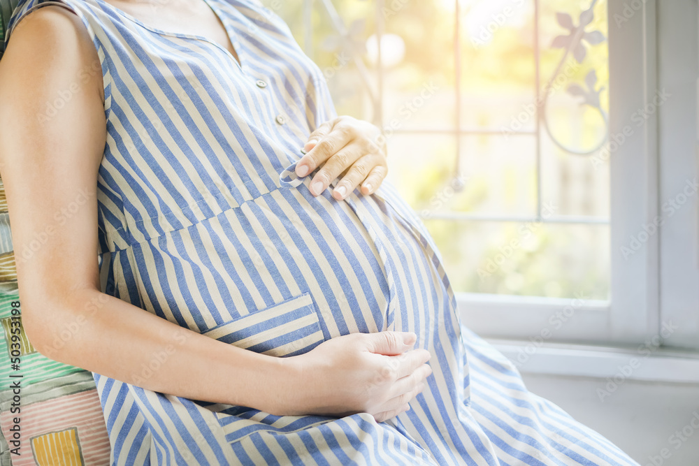 Pregnant woman touching her swollen belly and sitting near the window