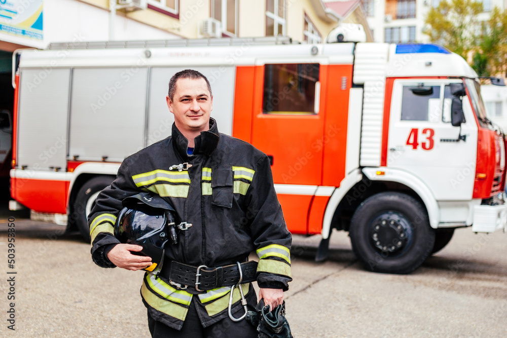 Firefighters man in a protective suit near fire truck. Protection, rescue from danger. Fire station Firefighters man in a protective suit near fire truck. Protection, rescue from danger. Fire station