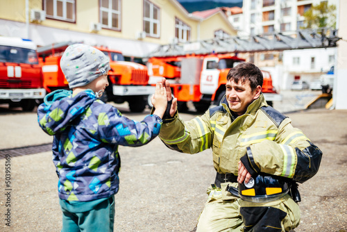 Foto Portrait of a firefighter with kid standing against the backdrop of fire trucks