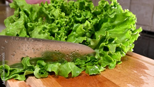 man with chef's knife cutting lettuce on wooden board