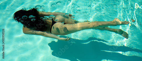Woman swimming underwater in a blue pool.