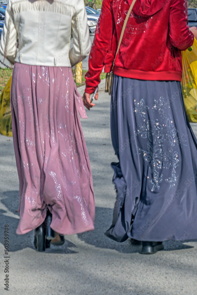 Two women in national dresses are shopping on the sidewalk on a spring day