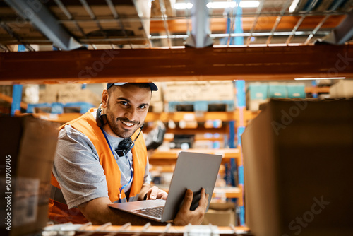 Happy warehouse worker using laptop and looking at camera. © Drazen