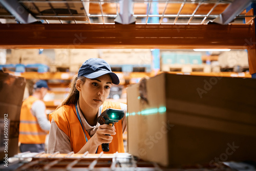 Female warehouse worker uses bar code reader while scanning packages at storage compartment. photo