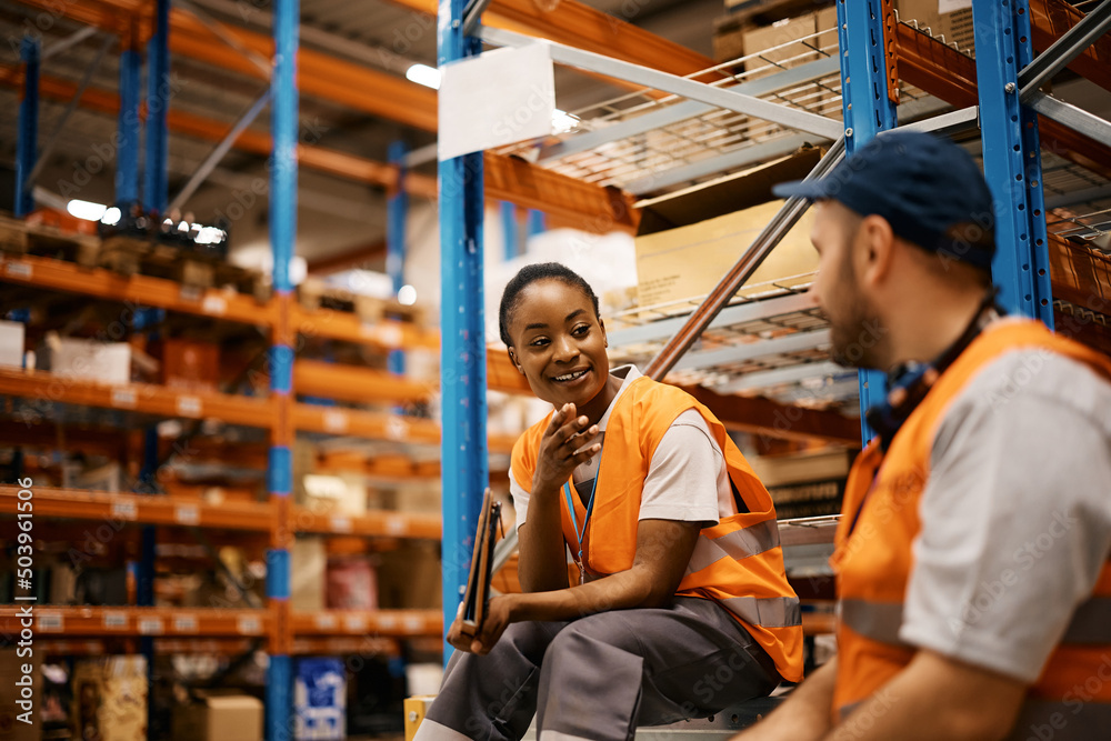 Happy African American worker and her colleague talk on break at distribution warehouse.