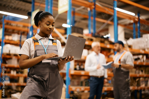Young black woman using laptop while working at distribution warehouse.