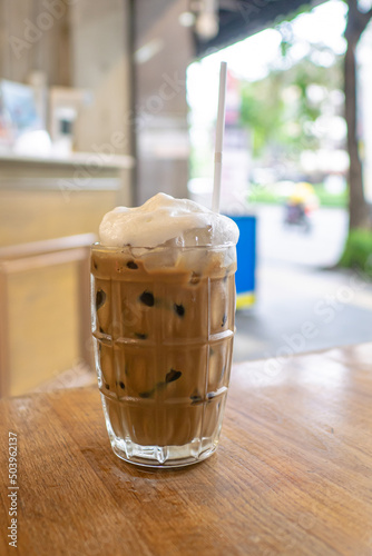 Thai iced coffee, a close up of glass of milk coffee cold drink beverage and white straw on wooden table at Thai food restaurant background in Bangkok, Thailand.