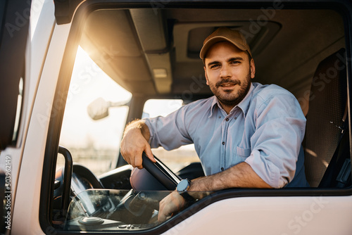 Young truck driver behind steering wheel in vehicle cabin looking at camera. photo