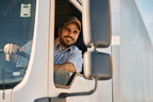 Fototapeta Happy professional truck driver driving his truck and looking at camera