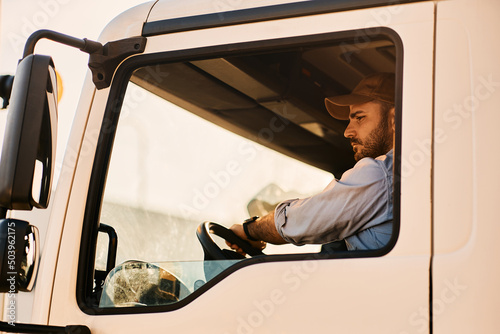 Slika na platnu Professional truck driver driving in reverse while looking in side view mirror