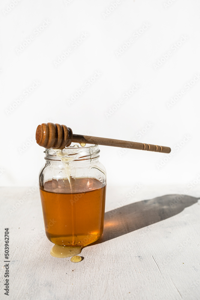 Glass jar with raw honey from bees with honey drops and honey spoon Glass jar with raw honey from bees with honey drops and honey spoon