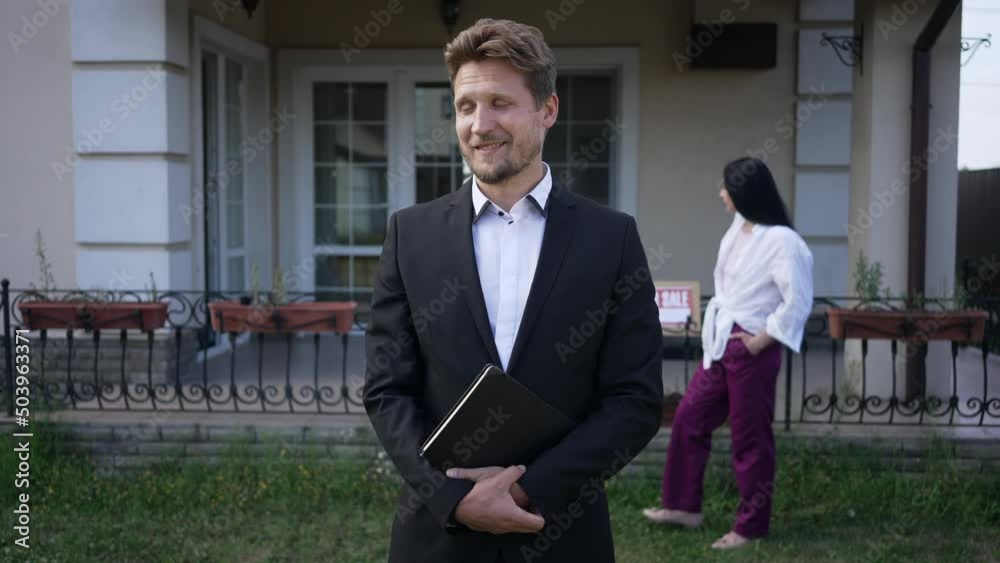 Smiling male seller looking back at buyer walking on backyard turning to camera. Portrait of confident positive Caucasian man in suit posing in slow motion outdoors selling new house Smiling male seller looking back at buyer walking on backyard turning to camera. Portrait of confident positive Caucasian man in suit posing in slow motion outdoors selling new house