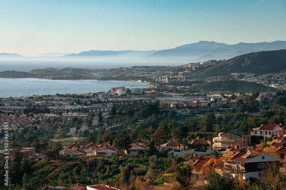 Panorama of Kusadasi city in Turkey with Long Beach and villas in the foreground and mountains and sea in background.