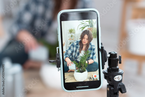 Woman making video how to repotting and watering plants using using smartphone at home