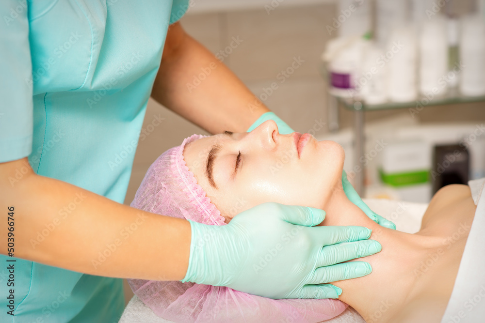 Naklejka premium Cosmetologist with gloved hands applies a moisturizing mask with peeling cream on the female face. Facial cosmetology treatment. Procedures for facial care