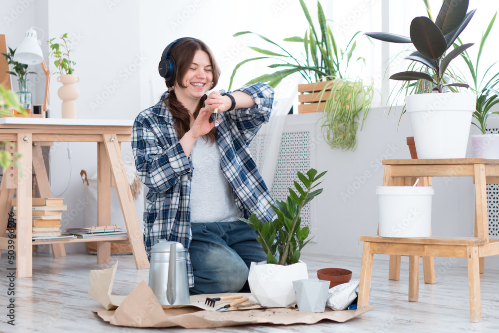 Woman moving plant to new pot and listening music using wireless headphones and smart watch at home