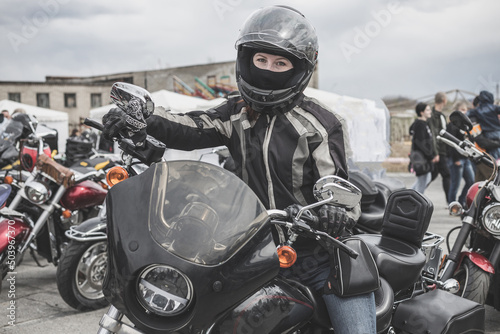 A young biker woman in a leather jacket and helmet on a motorcycle.