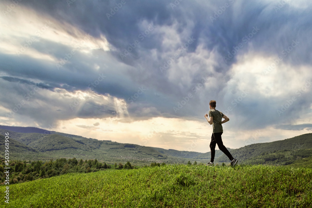 Male runner running from grass top of mountain hill. Healthy man jogging Male runner running from grass top of mountain hill. Healthy man jogging