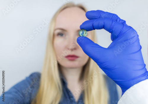 Fototapeta Naklejka Na Ścianę i Meble -  Conceptual shot of an eye crystalline lens replacement. Ophthalmic surgery. Return of sight. Removal of cataracts. Surgical intervention in the eyeball. Doctor holds the implant near the patient