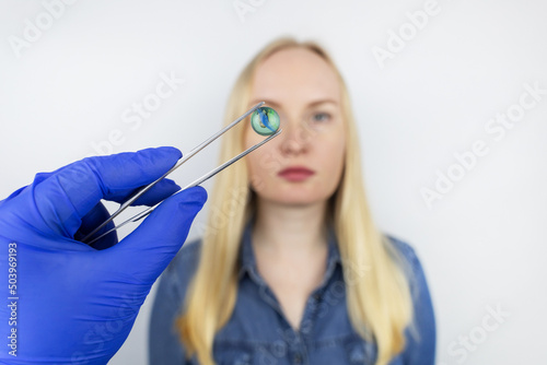 Conceptual shot of an eye crystalline lens replacement. Ophthalmic surgery. Return of sight. Removal of cataracts. Surgical intervention in the eyeball. Doctor holds the implant near the patient photo