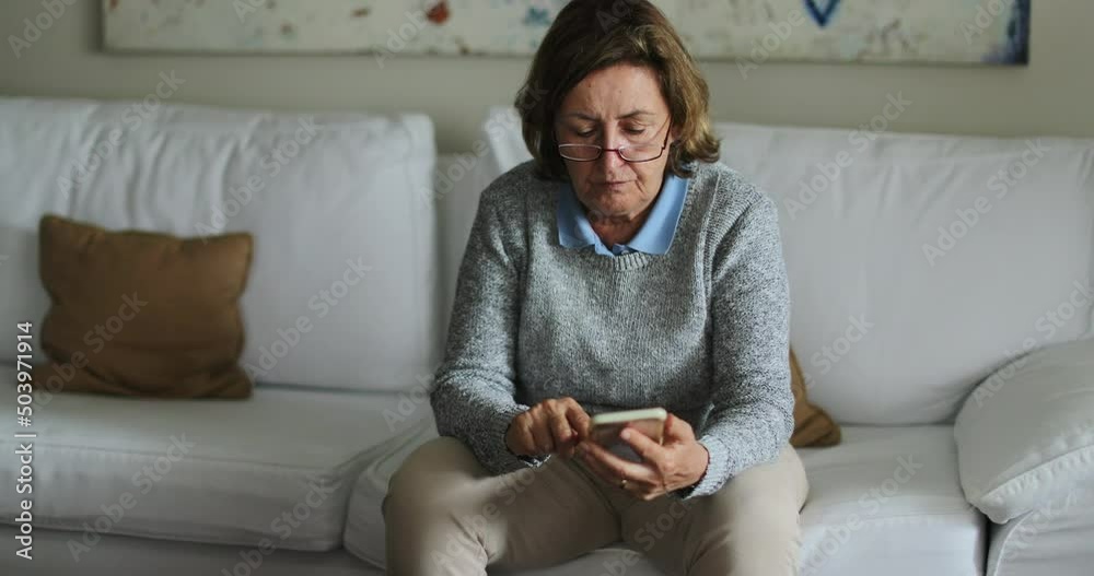 Senior woman using technology sitting on couch at home older person texting touching smartphone screen