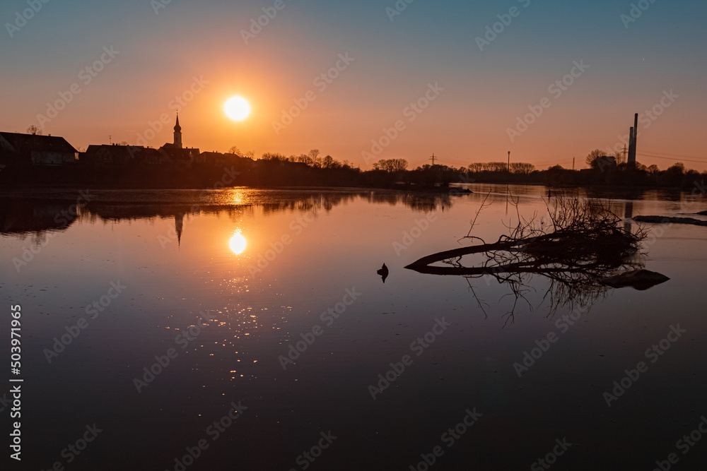 Beautiful sunset with reflections and silhouettes of a church and a power plant near Pleinting, Danube, Bavaria, Germany