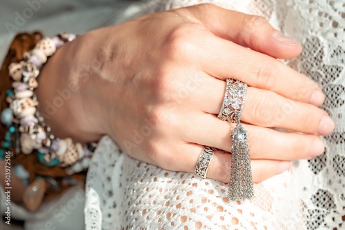 Close up of beautiful tribal boho style woman hands with lots of accessories. Boho style for fashionable look on resort. Middle aged well looking woman in white dress and boho style braclets.