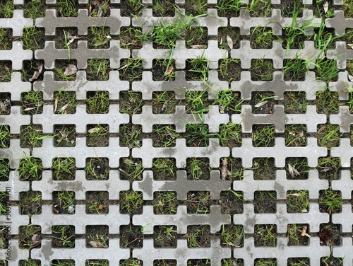 grass sprouting through holes in metallic gray tile as urban abstract natural backdrop, nature and urban space combination graphic resource, mixed texture full frame