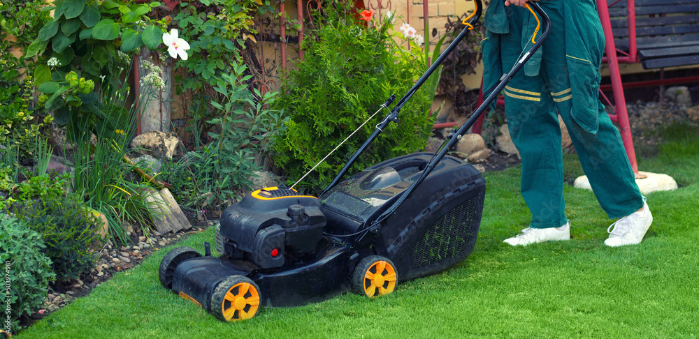 Fototapeta premium Young gardener mowing the lawn with lawnmower in summer