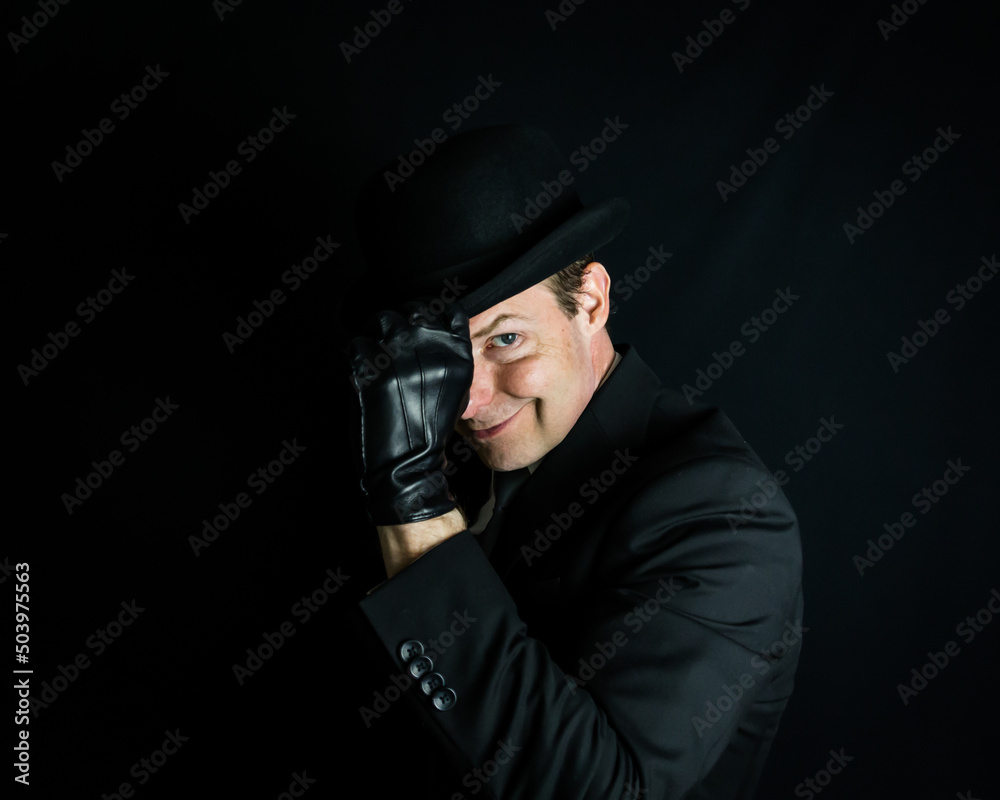 Portrait of British Businessman in Dark Suit and Leather Gloves Tipping Bowler Hat and Smirking. Concept of Film Noir Secret Spy Hero. Portrait of British Businessman in Dark Suit and Leather Gloves Tipping Bowler Hat and Smirking. Concept of Film Noir Secret Spy Hero.