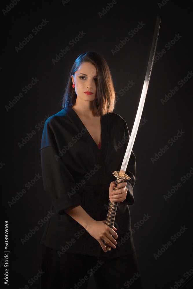 Portrait of a young brunette kung fu girl with a Japanese sword on a black background.