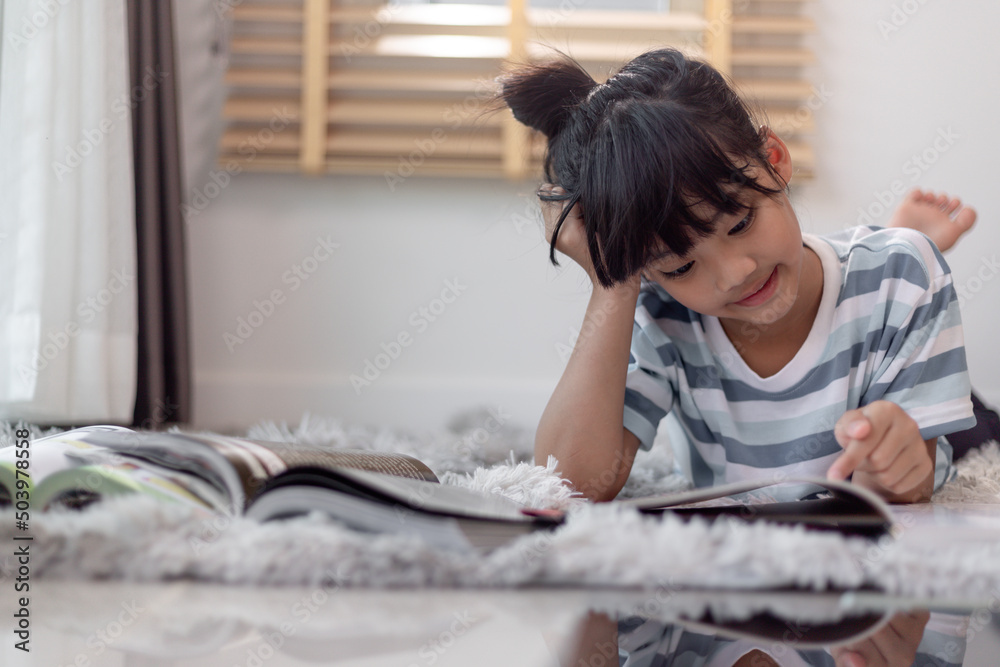 Child reading book at home. Girl lying and reading indoors Child reading book at home. Girl lying and reading indoors