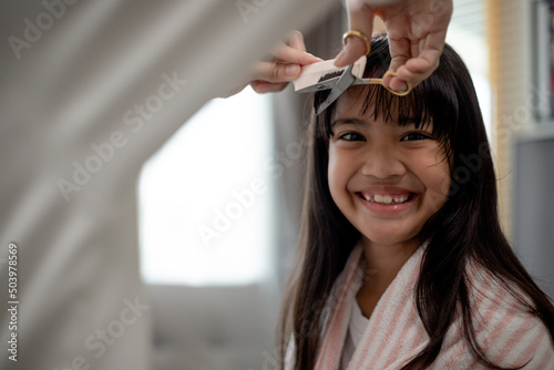Asian Mother cutting hair to her daughter in living room at home while stay at home safe from Covid-19 Coronavirus during lockdown. Self-quarantine and social distancing concept.