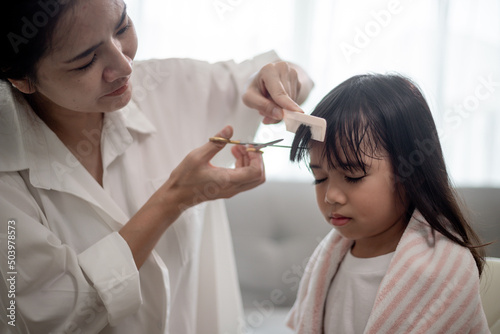 Asian Mother cutting hair to her daughter in living room at home while stay at home safe from Covid-19 Coronavirus during lockdown. Self-quarantine and social distancing concept.