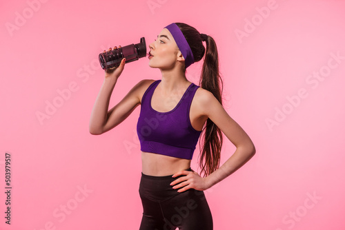 Sportswoman drinks water on pink background