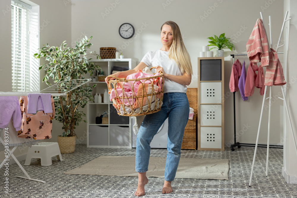 Young smiling blonde woman spends time at home doing housework, stands ...