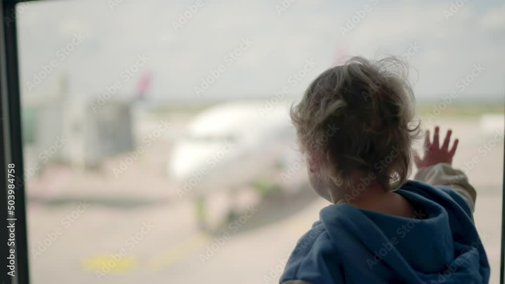 Little boy watching planes at the airport standing in silhouette with his back to the camera at a large window overlooking the tarmac Little boy watching planes at the airport standing in silhouette with his back to the camera at a large window overlooking the tarmac