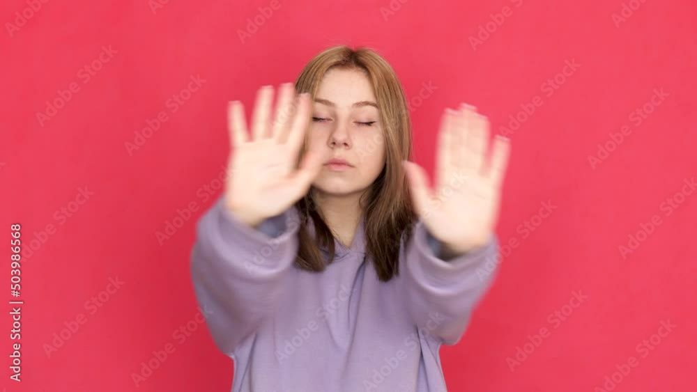 Caucasian serious young woman 20 years old shows a gesture with her hands don't stop, caution. The girl gestures to cancel, calm down. Studio shooting, red background Caucasian serious young woman 20 years old shows a gesture with her hands don't stop, caution. The girl gestures to cancel, calm down. Studio shooting, red background