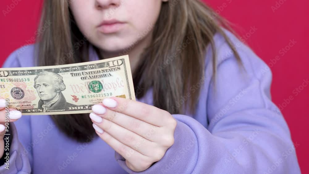 close-up Caucasian young woman 20 years old examines a bill of 10 US dollars. Girl holding 10 American dollars cash in her hands.Selective focus close-up Caucasian young woman 20 years old examines a bill of 10 US dollars. Girl holding 10 American dollars cash in her hands.Selective focus